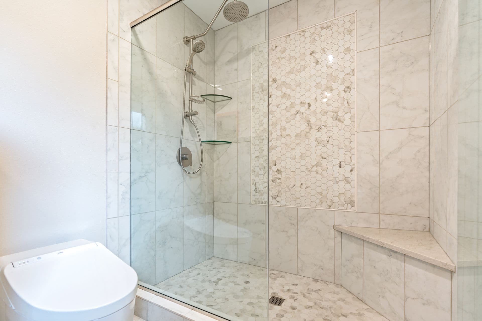 An off-white multi-style tiled walk in shower with a built-in corner bench and sliding glass doors.