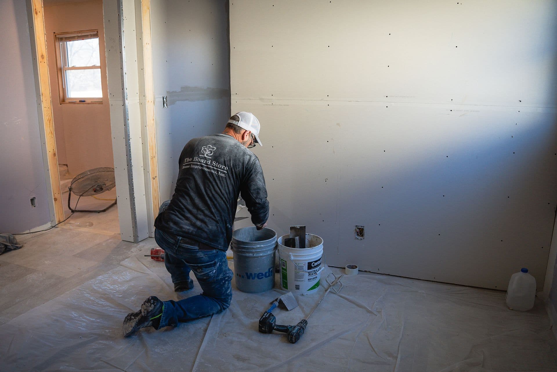 A worker installs drywall for a bathroom renovation.